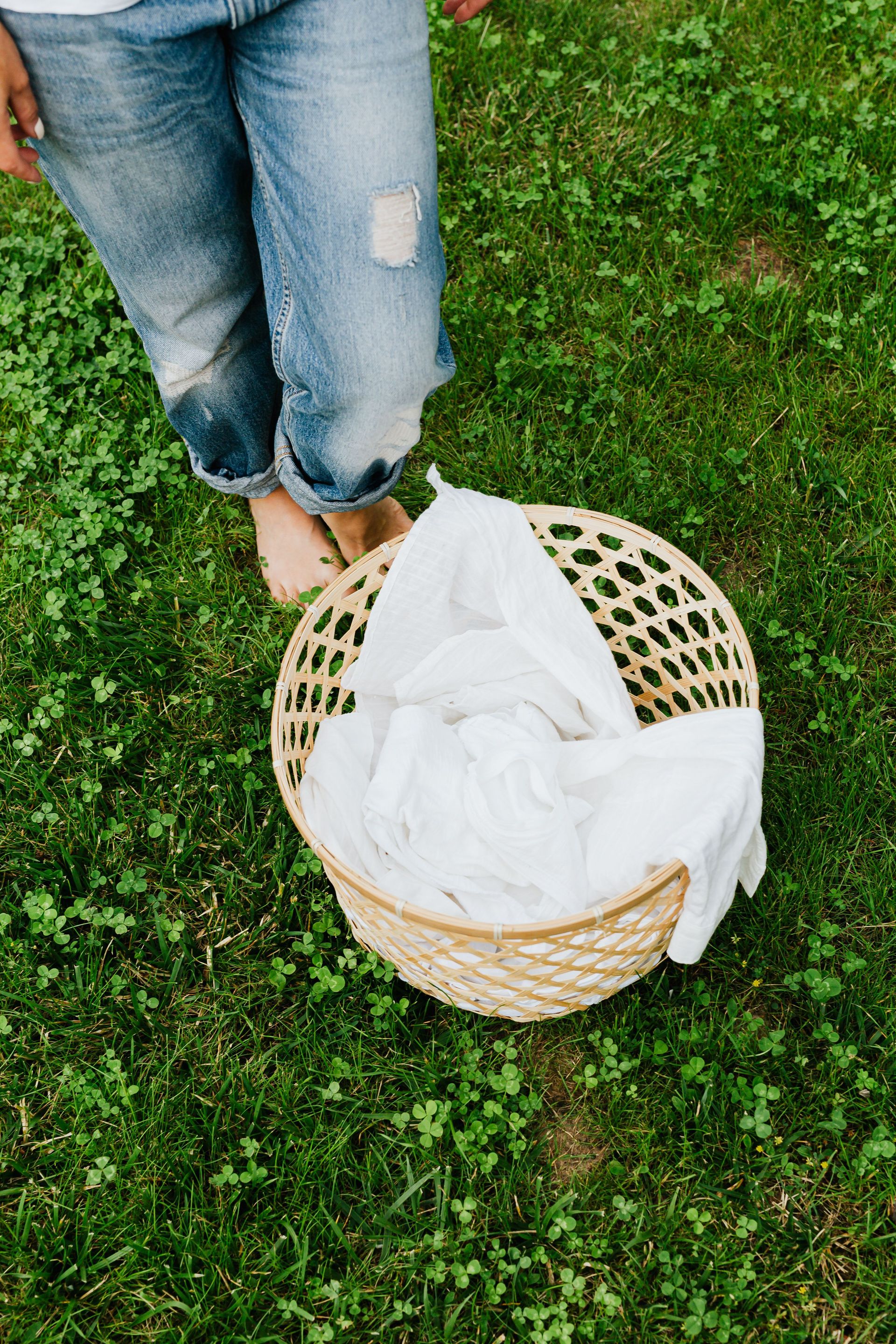 Close-up of a person standing barefoot on grass with a laundry basket.