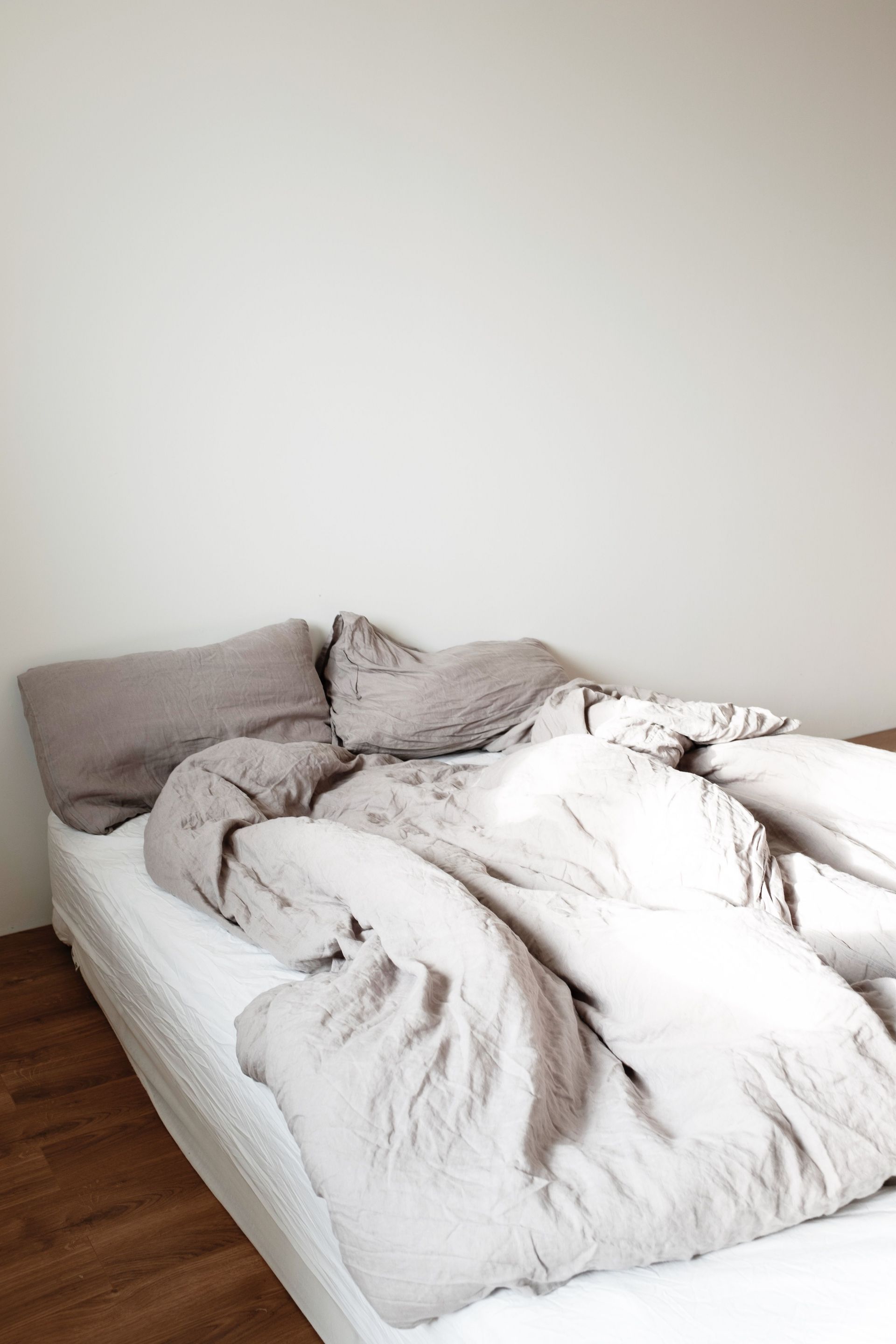 Experience the simplicity and warmth of a cozy unmade bed in a minimalist bedroom setting.