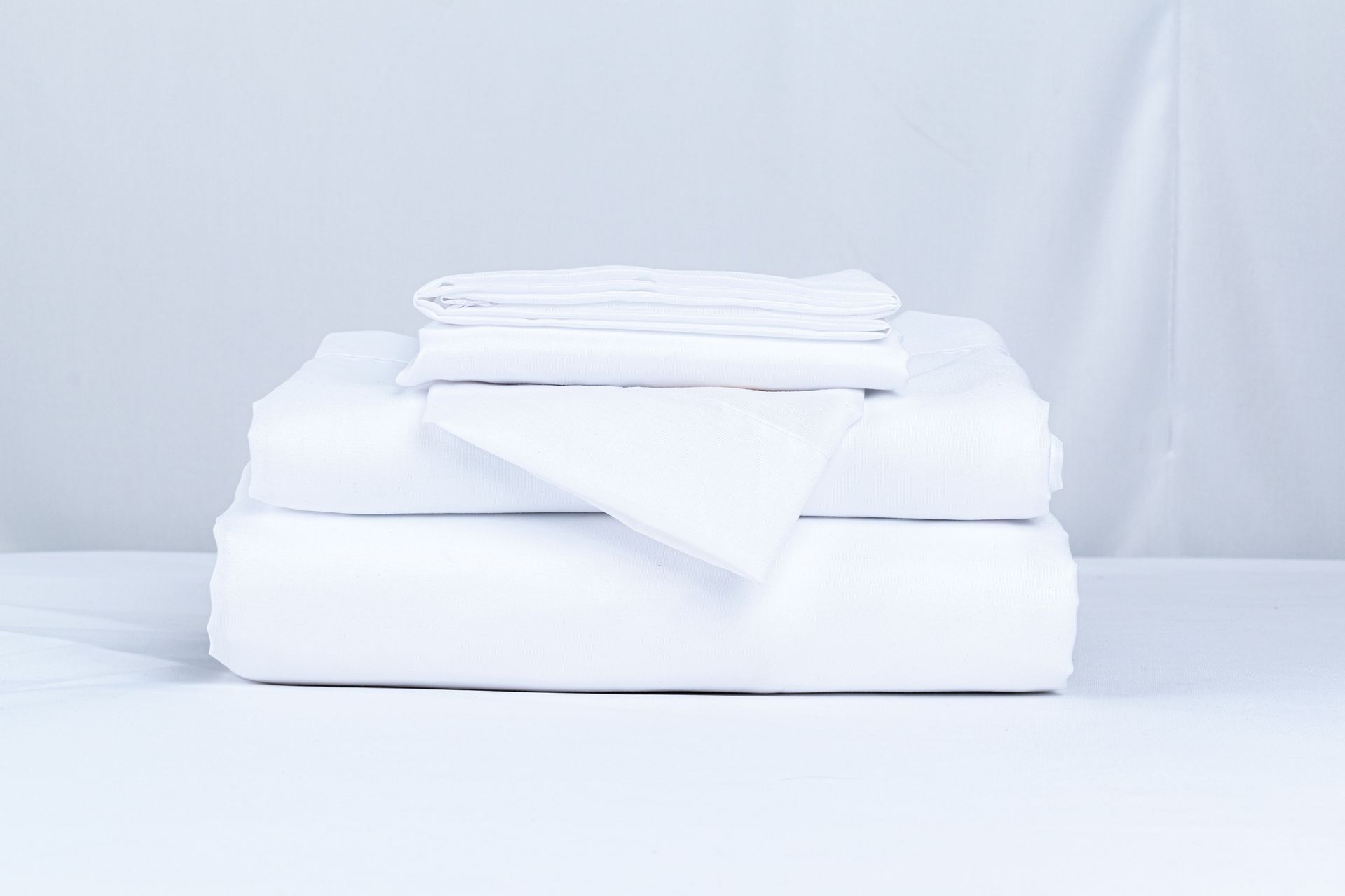 A neatly folded stack of crisp white bed linens on a clean surface.