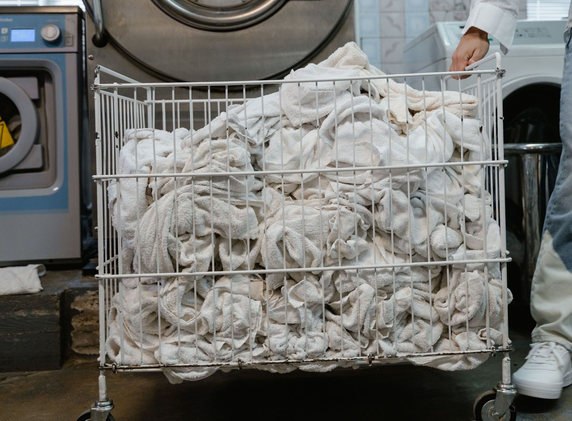 A worker handling a cart of white linens in an industrial laundry setting.